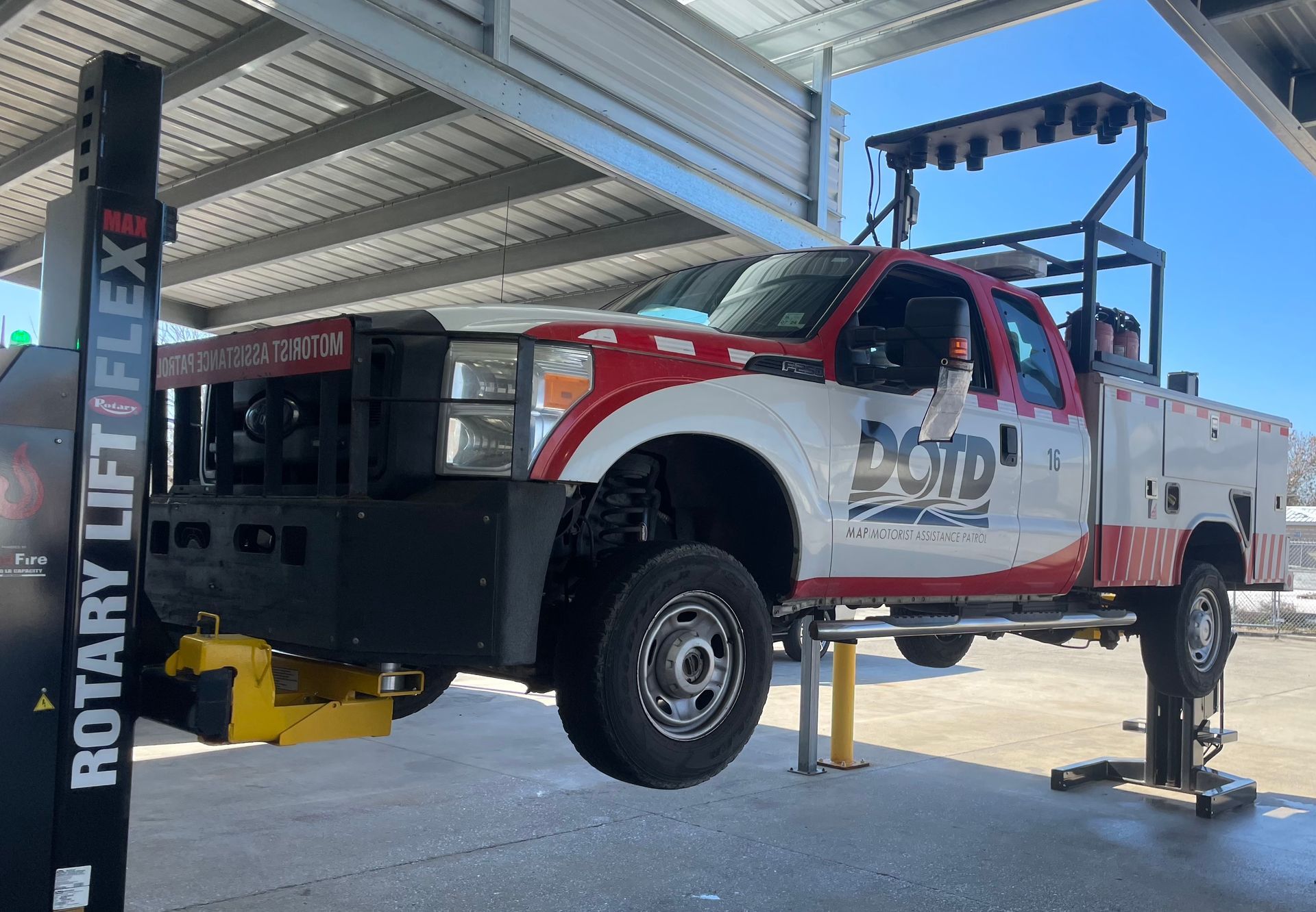 Red and white lifted utility truck on a hoist in a workshop, with the front bumper removed.