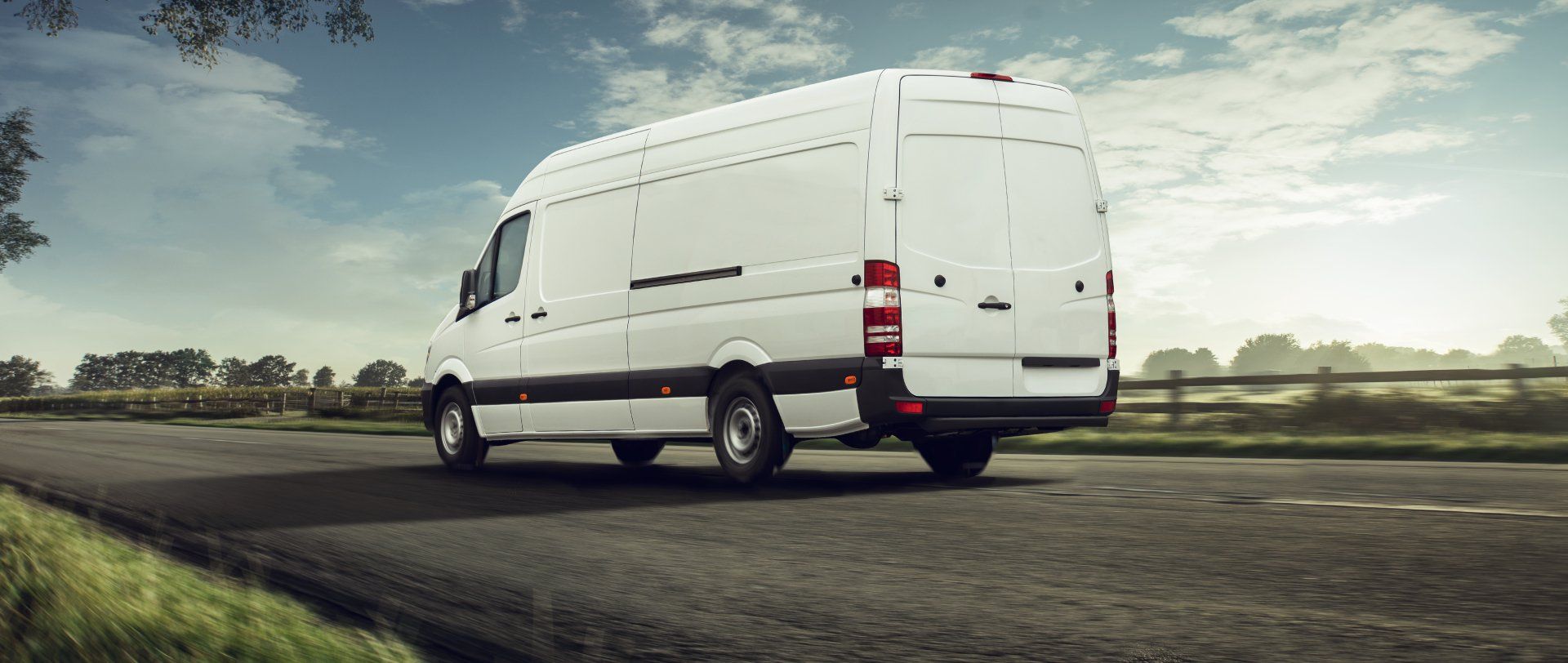 A white cargo van driving along a road through a rural landscape.