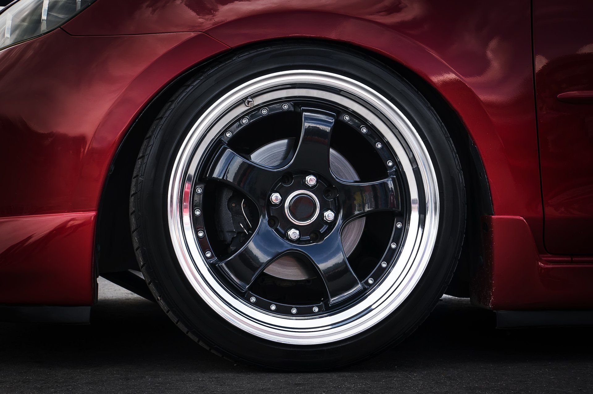 A close-up of a glossy black car wheel with a polished silver rim mounted on a deep red car body.