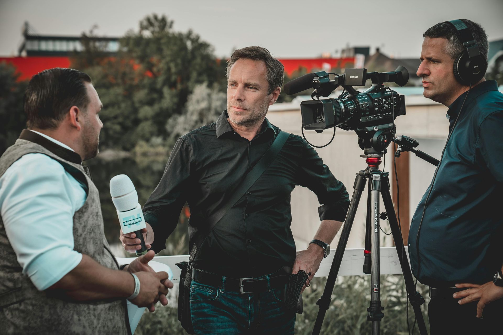 Three men are standing in front of a camera talking to each other.