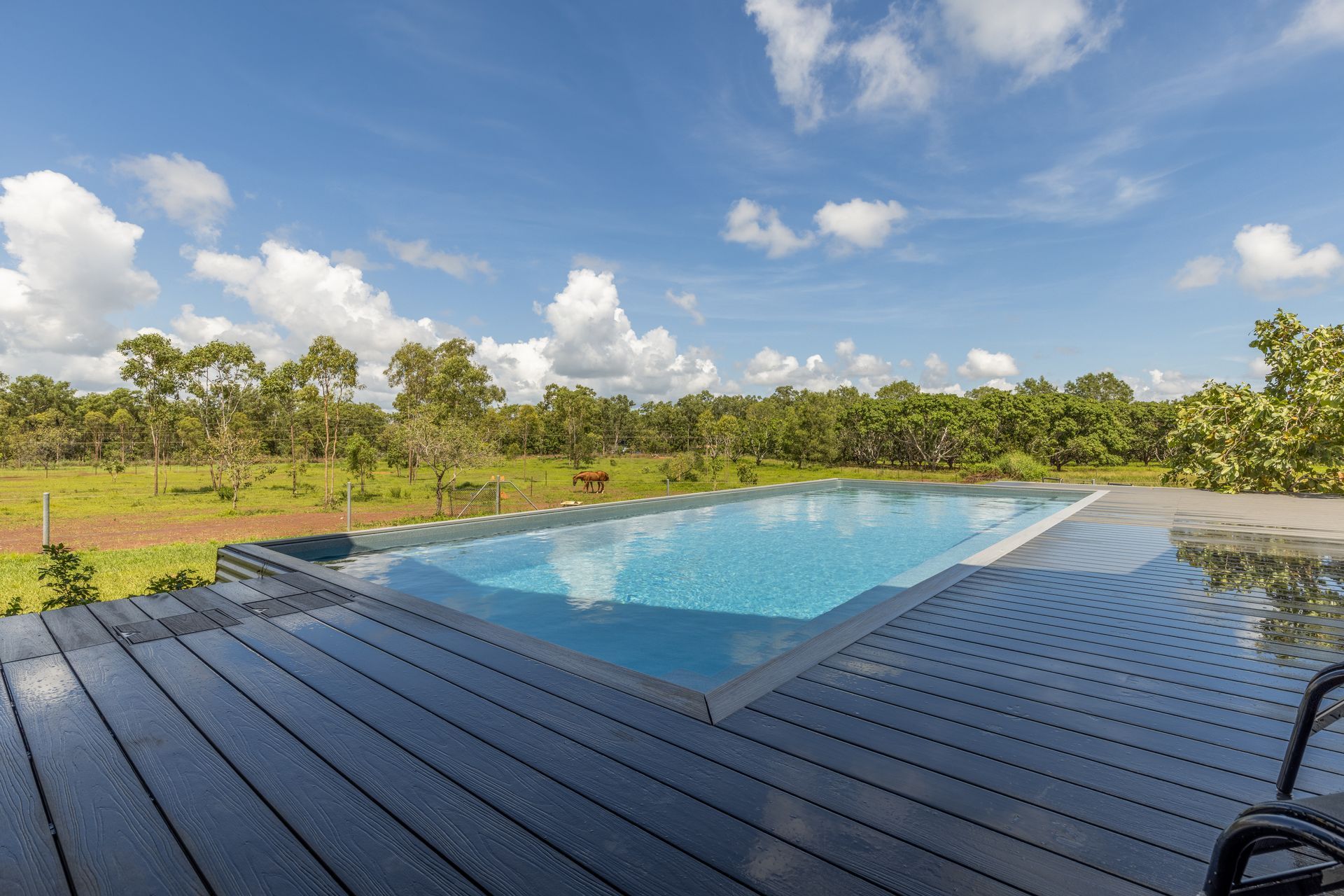 A Large Swimming Pool Is Surrounded by Trees and A Wooden Deck — Pooltech NT In Alawa, NT