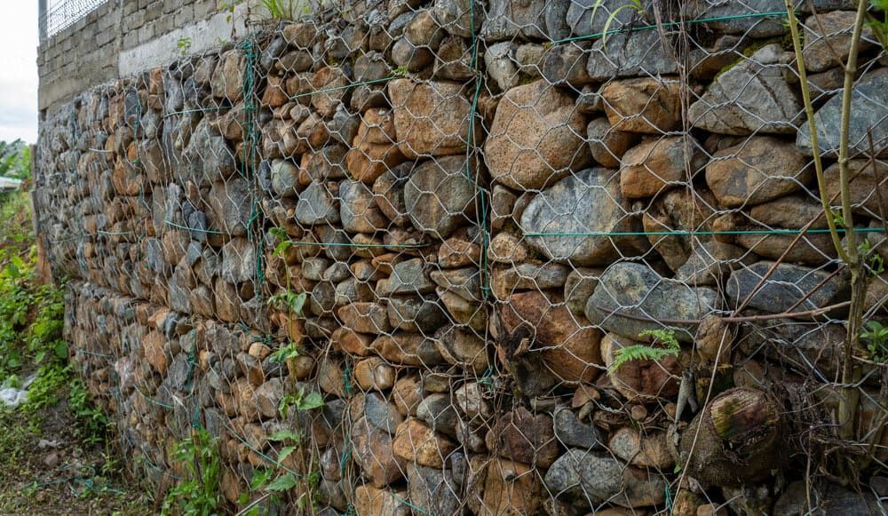 Stone Wall Built With Rocks Held in a Wire Mesh — BC Earthmoving & Civil Construction in East Barron QLD