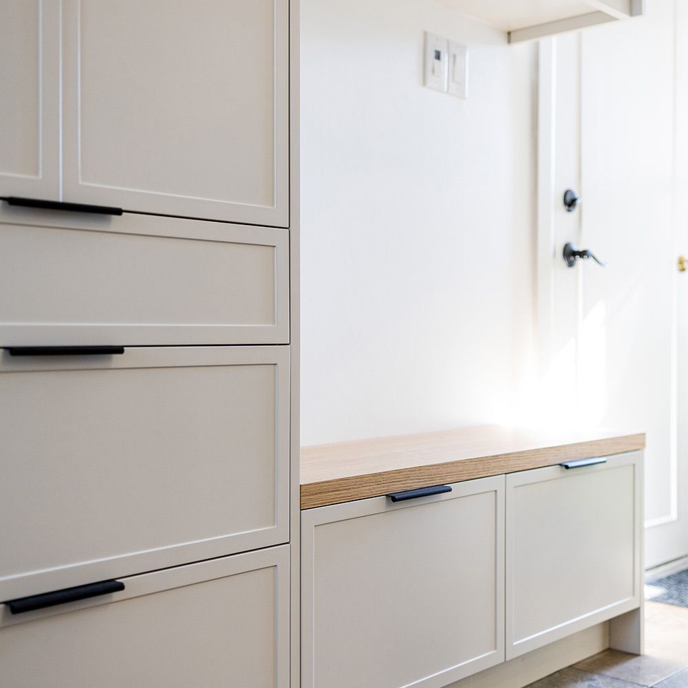 White built-in cabinets and bench storage in a bright entryway with a wooden top and black handles