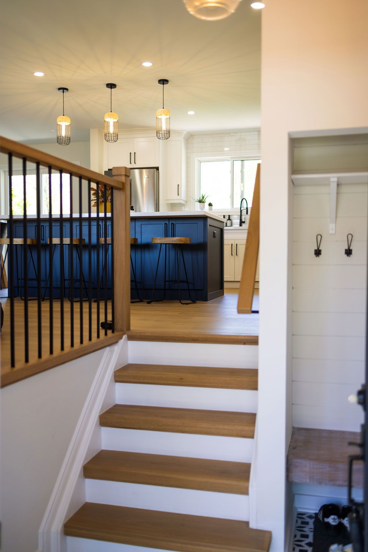 Staircase leading to a kitchen with a blue island and pendant lights. Entryway with coat rack.