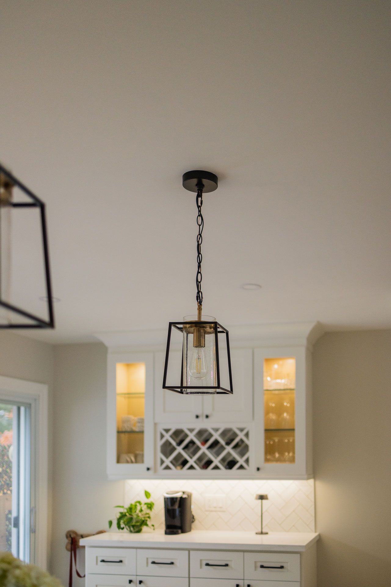 Black pendant light hangs above white cabinets in a kitchen.