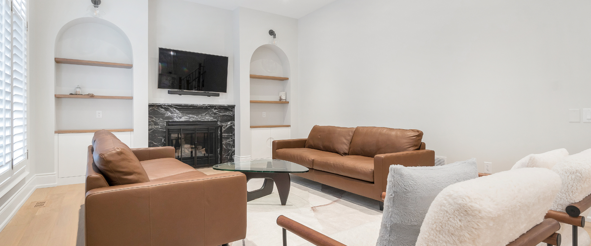 Bright living room with fireplace, built-in shelves, and large windows overlooking trees and a house.