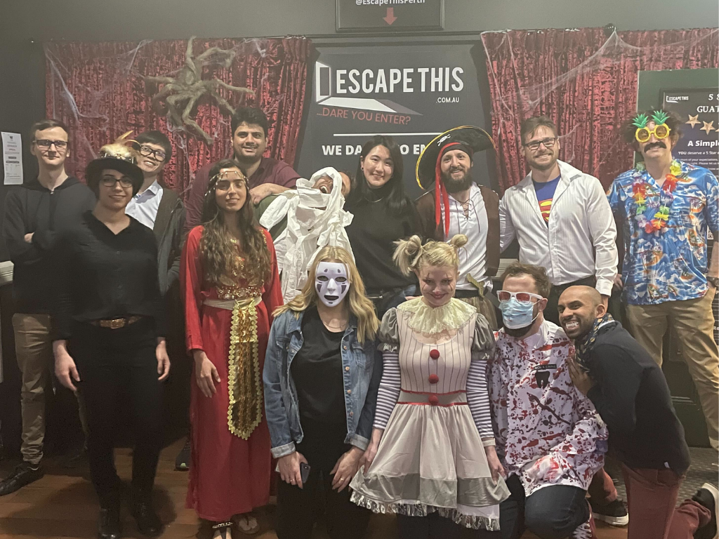 A group of people are posing for a picture in front of a sign that says escape this.