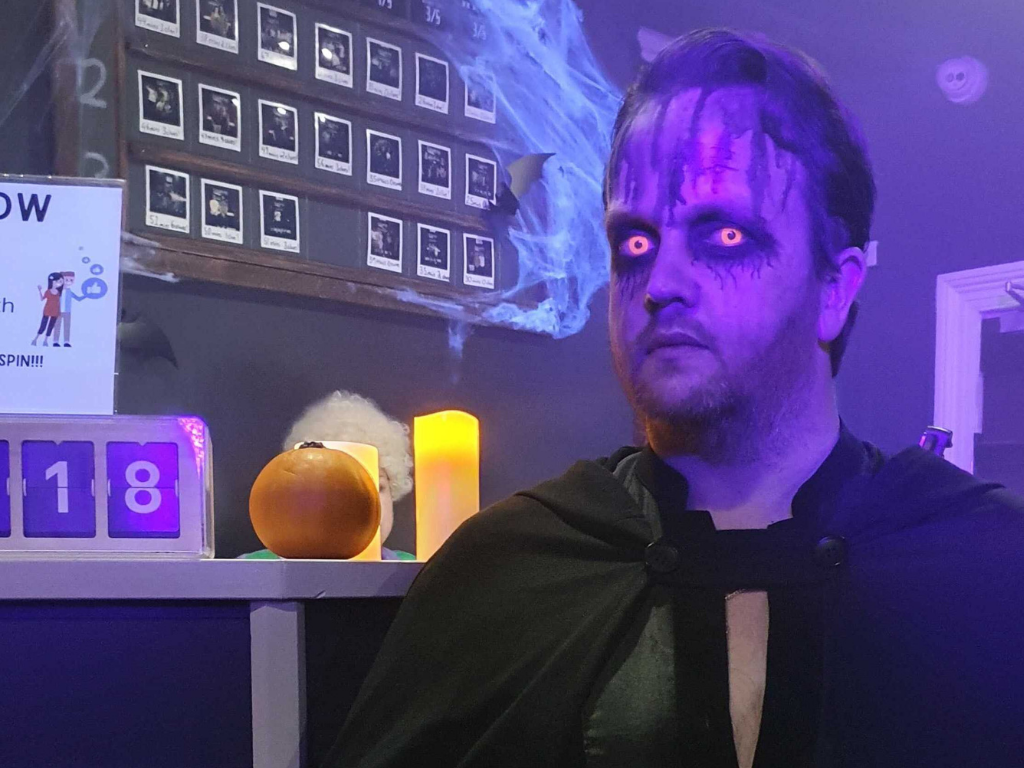 A horror escape room GM is dressed up for Halloween with glowing orange eyes