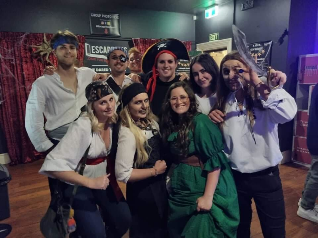 A group of escape room players in pirate costumes are posing for a photo.