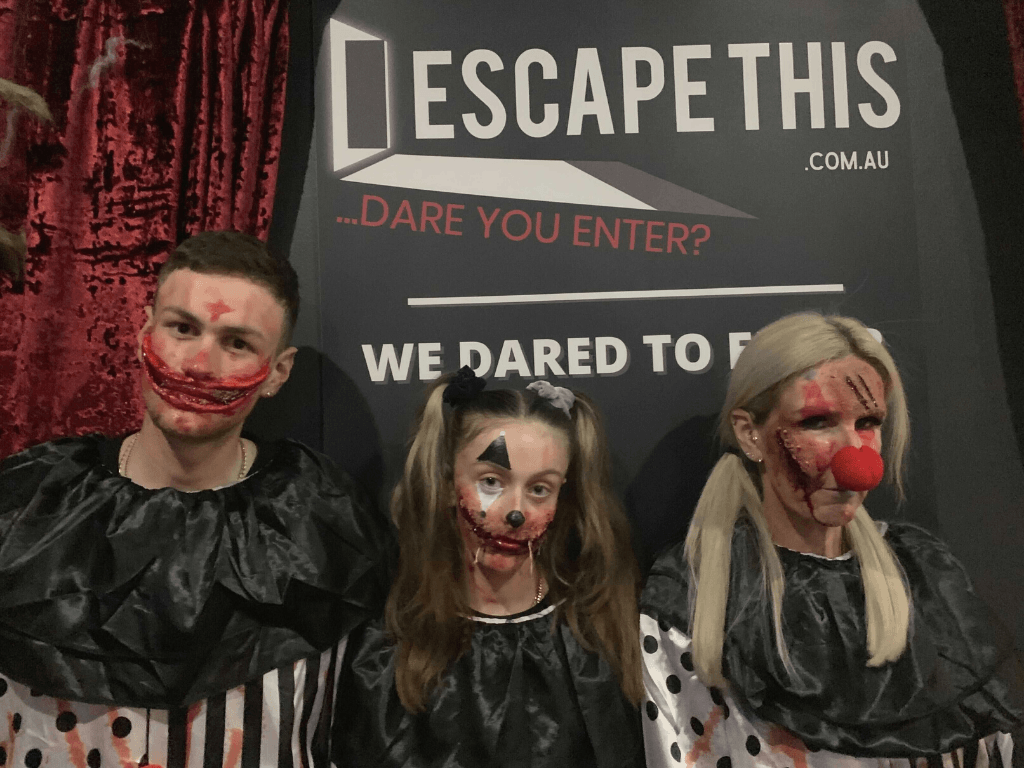 Three escape room players in gory Halloween makeup are posing for a photo