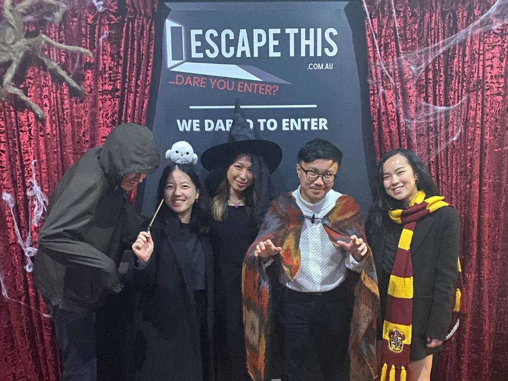 A group of people are posing for a picture in front of a sign that says `` escape this ''.