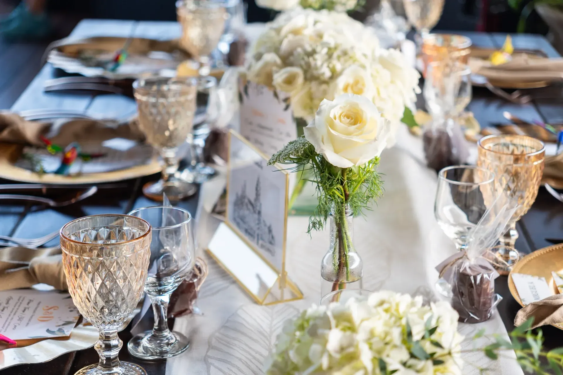 Elegante mesa puesta con flores blancas, copas con borde dorado y tarjetas de sitio.