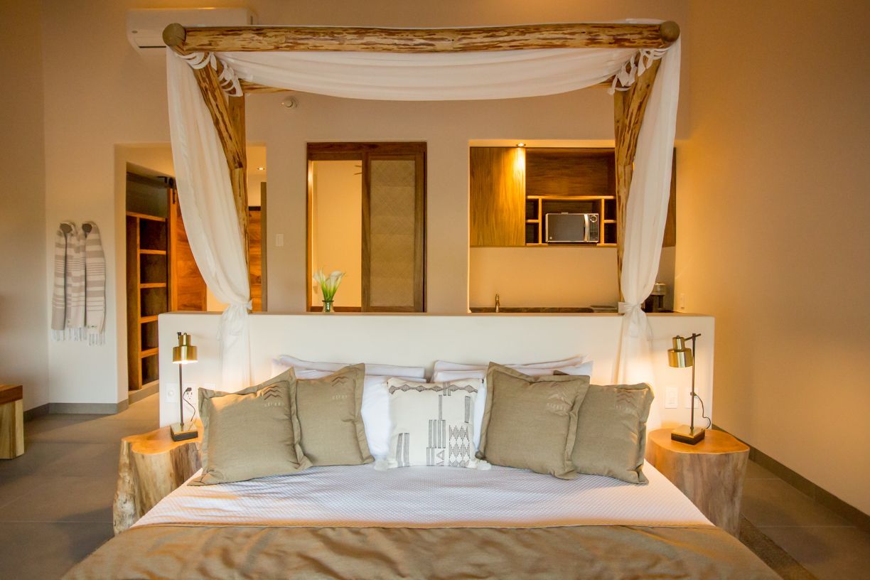Dormitorio con cama con dosel, esquema de colores neutros y pequeña cocina.