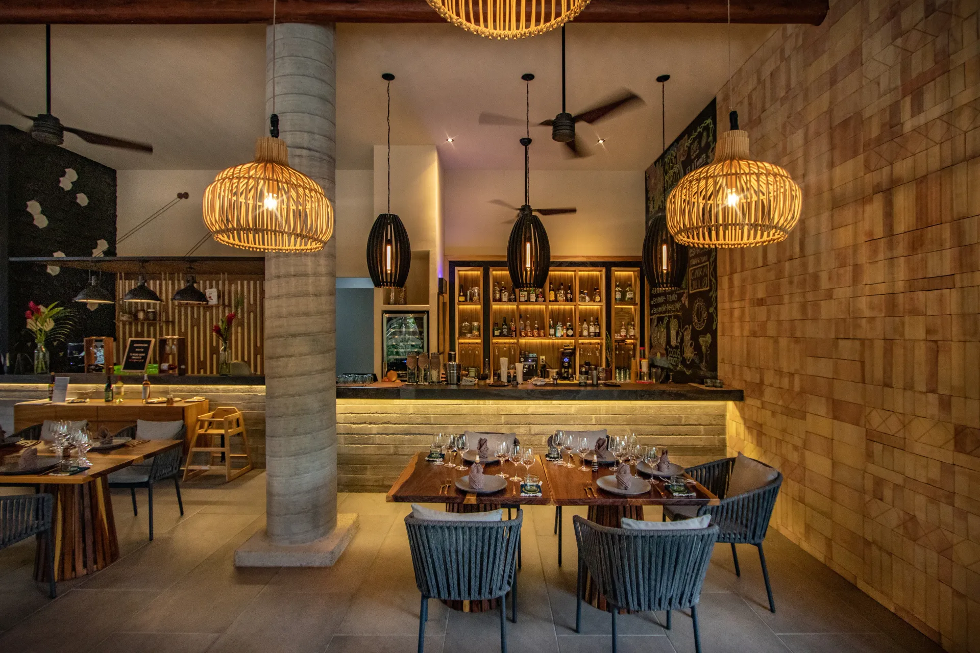 Interior del restaurante con lámparas colgantes, barra, mesas y paredes de piedra.