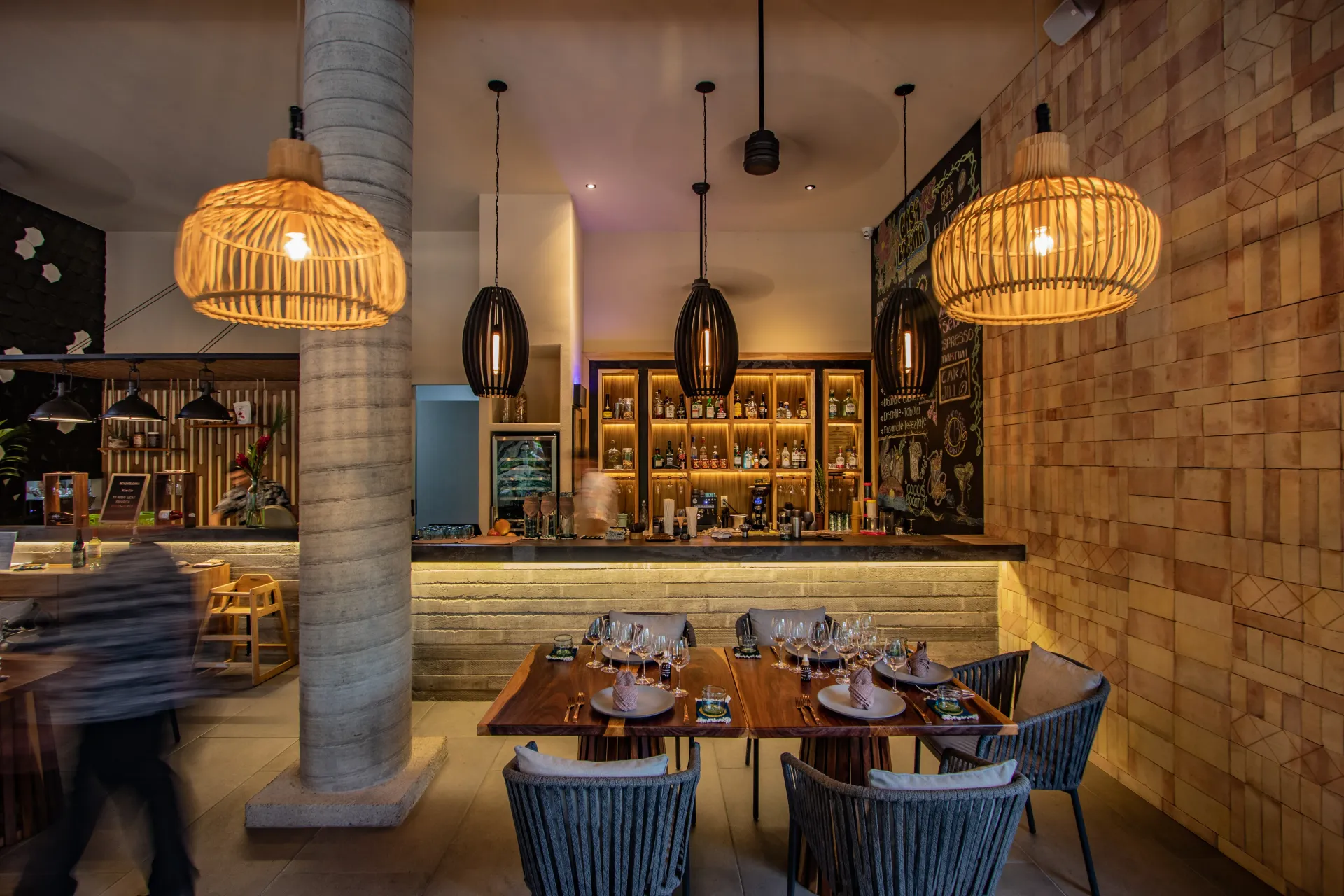 Interior del restaurante con barra, mesas y lámparas de mimbre.