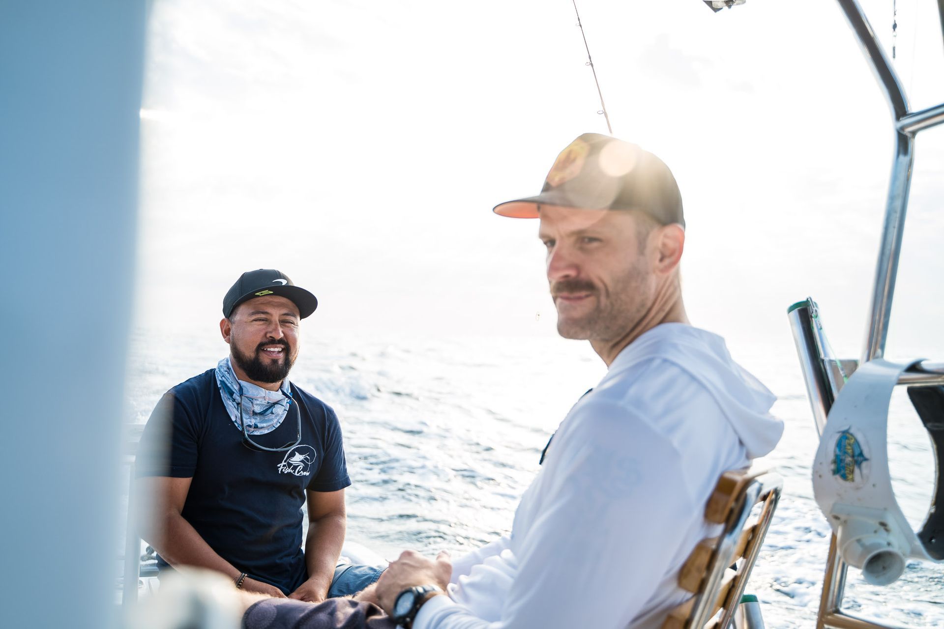 Dos hombres en un barco, uno con gorra y el otro con pañuelo, mirando hacia el océano.