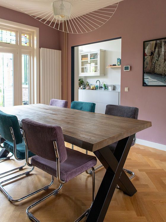 Eetkamer met een houten tafel, kleurrijke stoelen en uitzicht op de keuken.