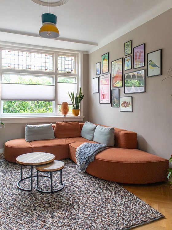 Woonkamer met oranje hoekbank, kleine salontafels, kunst aan de muur en een vloerkleed met patroon.