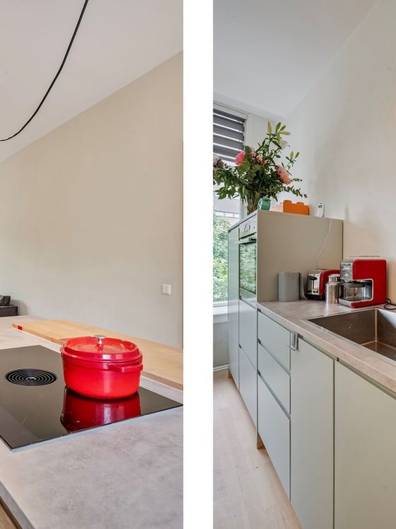 Moderne keuken met rode pan op het fornuis, lichte keukenkastjes en een bloemstuk.