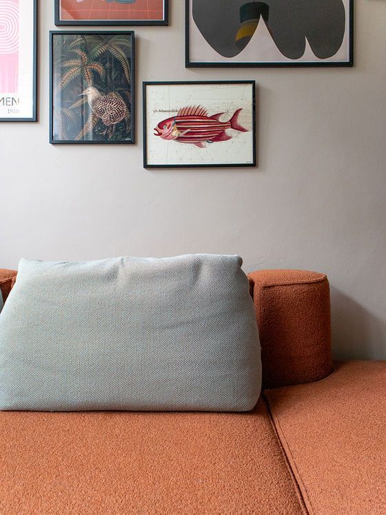 Oranje bank met grijs kussen, ingelijste kunst aan beige muur.