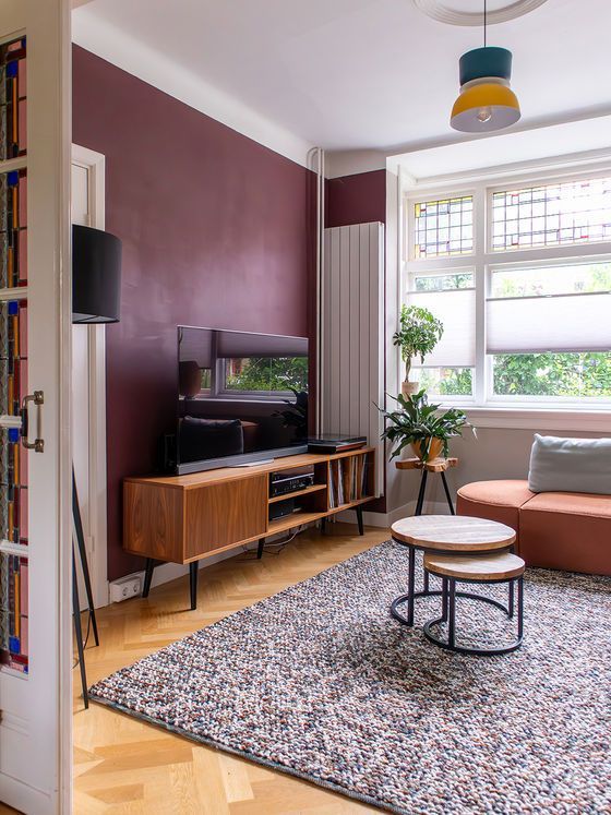 Woonkamer met een bordeauxrode muur, een houten tv-meubel en een vloerkleed met patroon.