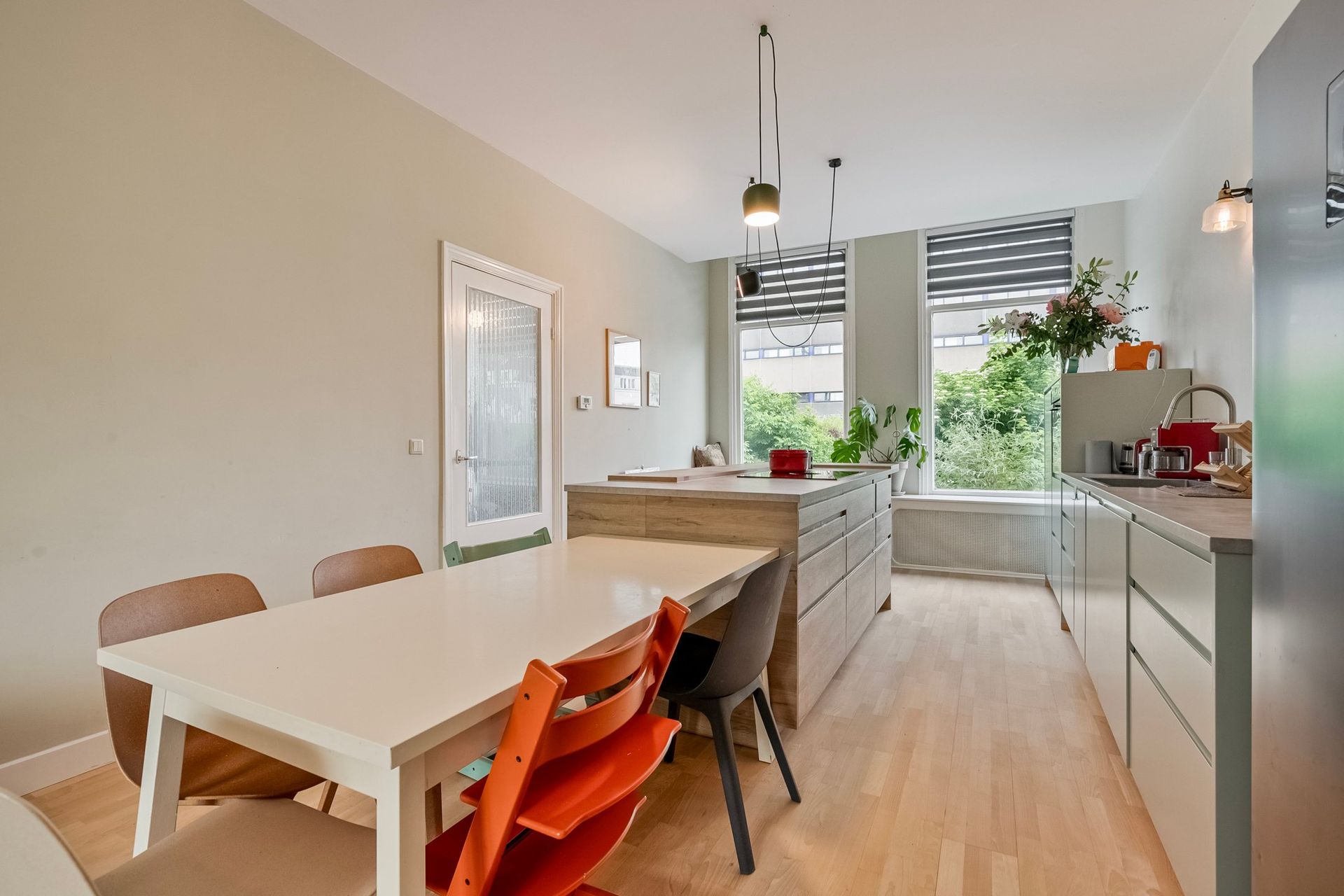 Moderne keuken met een witte eettafel, kookeiland en grote ramen.