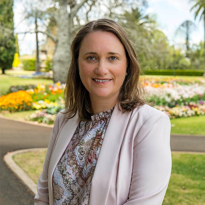 Woman in a light pink blazer standing in a flower garden, smiling at the camera.
