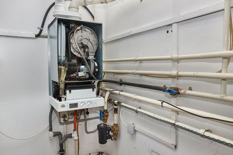 A boiler is sitting in a room next to pipes.
