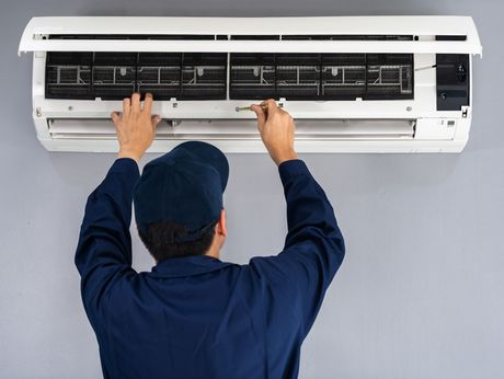 A man in a blue uniform is working on an air conditioner.