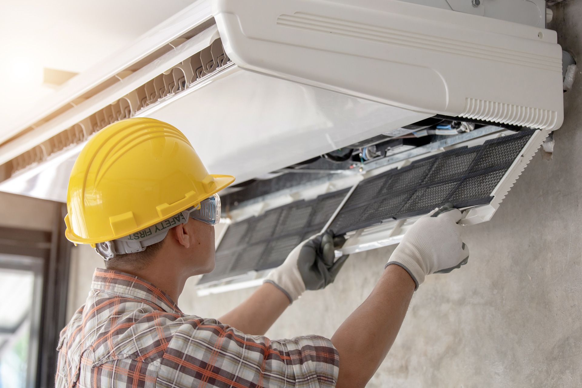 A man wearing a hard hat and gloves is cleaning an air conditioner.