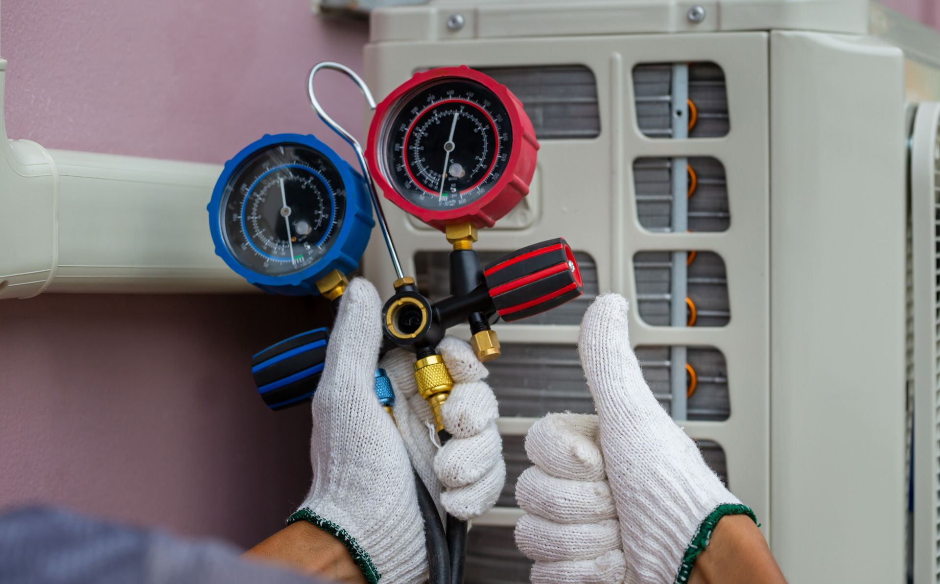 A person is holding two gauges in front of an air conditioner.