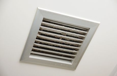 A dirty air vent on the ceiling of a room.