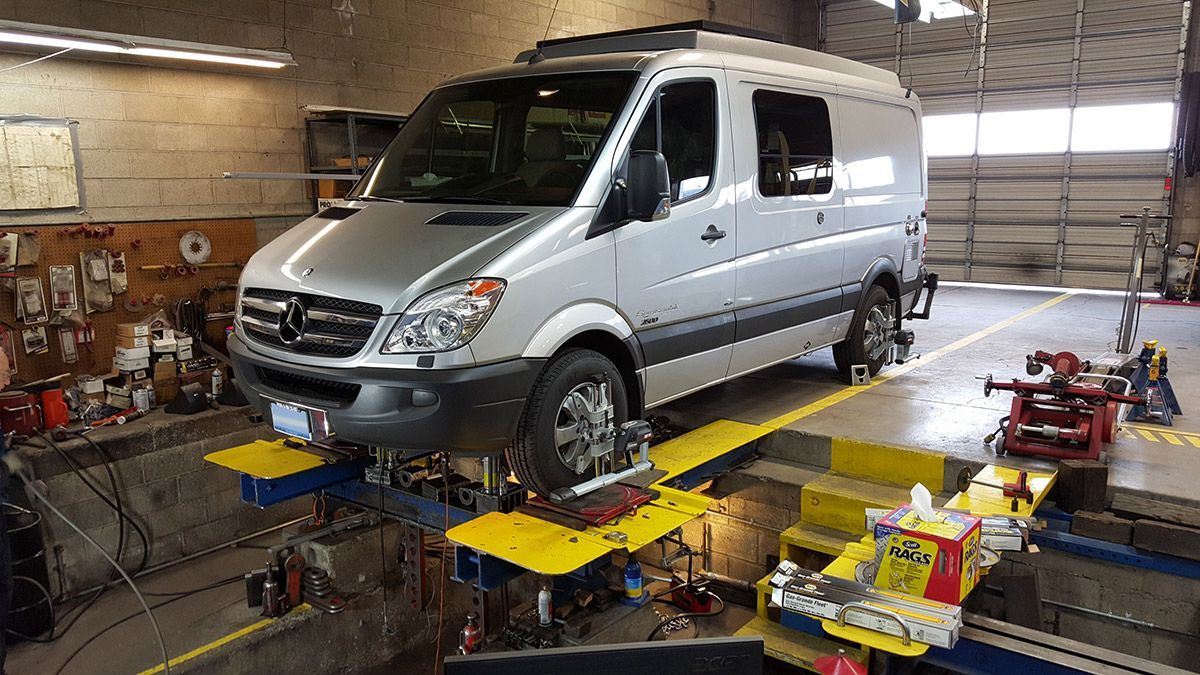 Silver van on a maintenance lift in an auto repair shop with tools and equipment around it | Sunshine Service Automotive Specialists