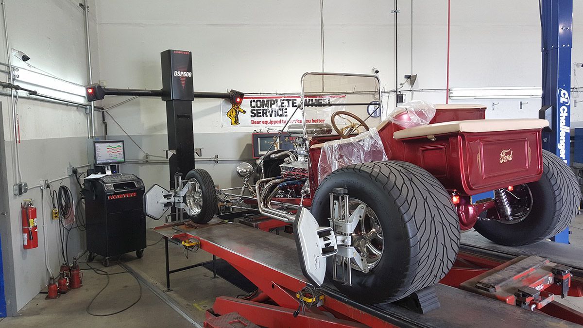 Red sports car on an alignment lift in an auto shop, with large rear wheels visible. | Sunshine Service Automotive Specialists