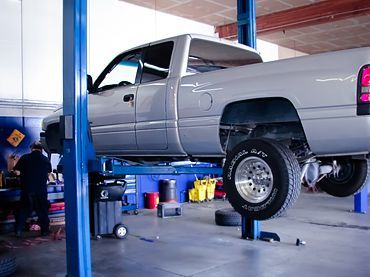 Silver pickup truck raised on a lift in an auto repair shop | Sunshine Service Automotive Specialists