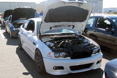 White sedan with hood open at a car show, engine exposed, parked among other modified cars | Sunshine Service Automotive Specialists