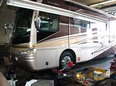 Large beige and silver motorhome parked inside a garage with tools and boxes nearby | Sunshine Service Automotive Specialists