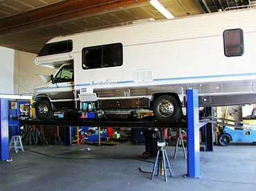 White RV on a lift inside an auto repair shop | Sunshine Service Automotive Specialists