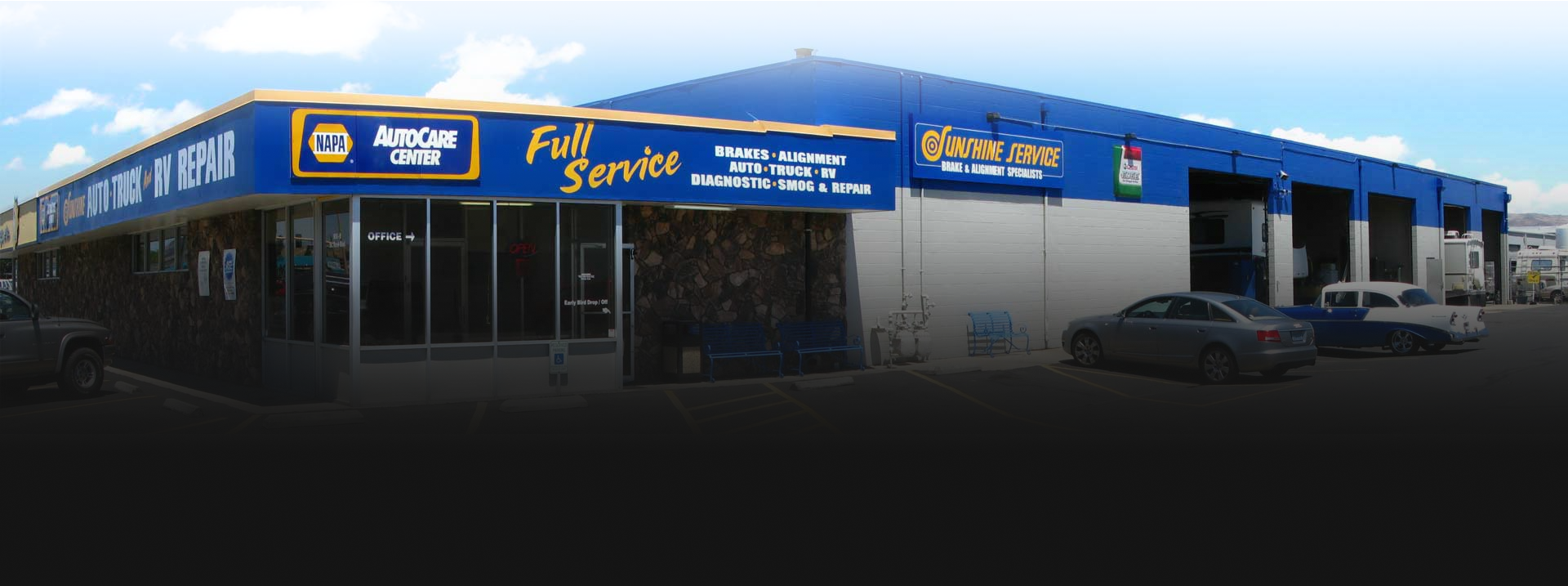 Blue auto repair shop exterior with signage and parked cars under a clear sky | Sunshine Service Automotive Specialists