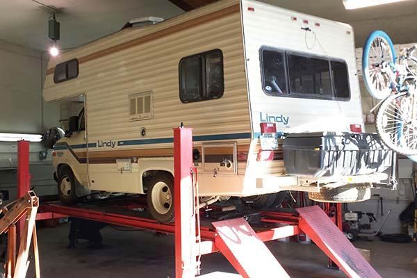 Vintage beige RV on a red hydraulic lift in a garage workshop | Sunshine Service Automotive Specialists