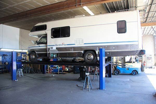 Large white camper van lifted on a blue hydraulic hoist in an auto repair garage. | Sunshine Service Automotive Specialists