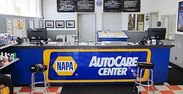 Auto repair shop counter with blue NAPA AutoCare Center sign and service area behind it | Sunshine Service Automotive Specialists