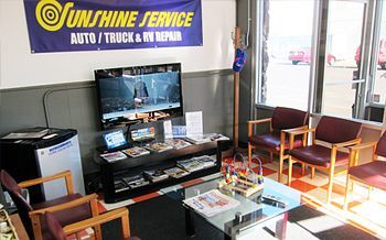 Waiting area in an auto repair shop with TV, chairs, coffee table, and sunlight through windows | Sunshine Service Automotive Specialists
