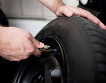 Hands inflating a black tire with a valve tool or air chuck | Sunshine Service Automotive Specialists
