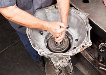 Mechanic installing a transmission clutch inside a car’s bell housing | Sunshine Service Automotive Specialists