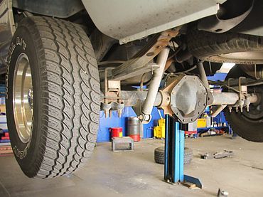 Undercarriage of a truck on a lift in a garage, with tires and suspension visible. | Sunshine Service Automotive Specialists