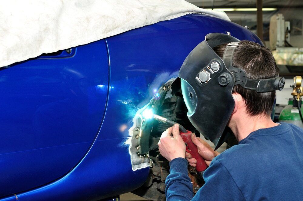 A Man Wearing a Welding Mask is Working on a Blue Car — M & D Shipp Smash Repairs In Dubbo, NSW