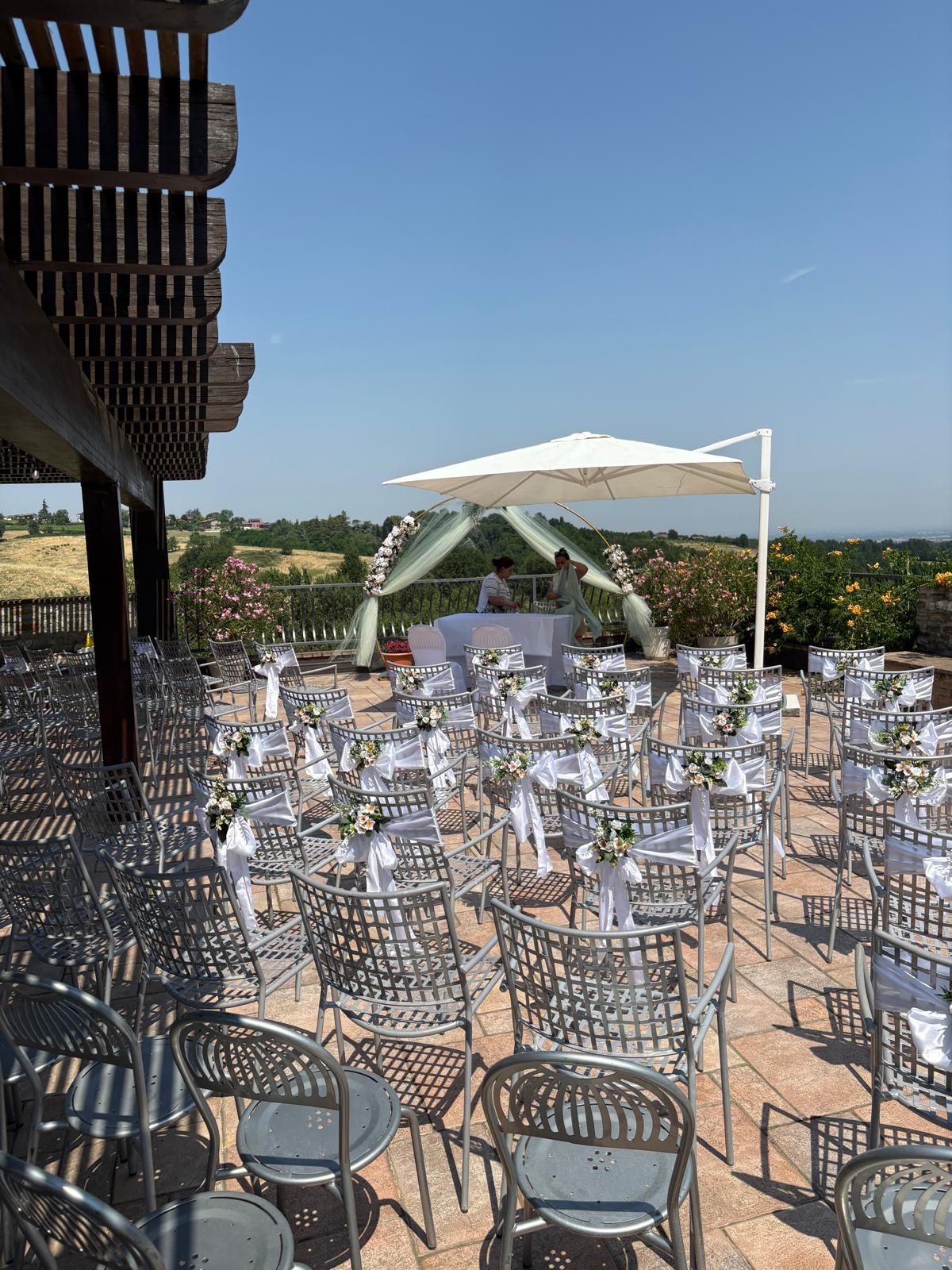 Ricevimento di nozze all'aperto con gazebo bianco, sedie argentate e vista panoramica sulla collina.