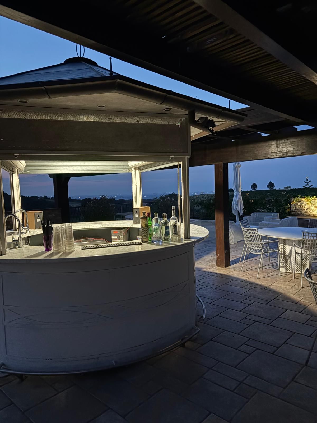 Un bar sulla spiaggia sotto un gazebo al tramonto, con sedie e tavoli bianchi che si affacciano sull'oceano.
