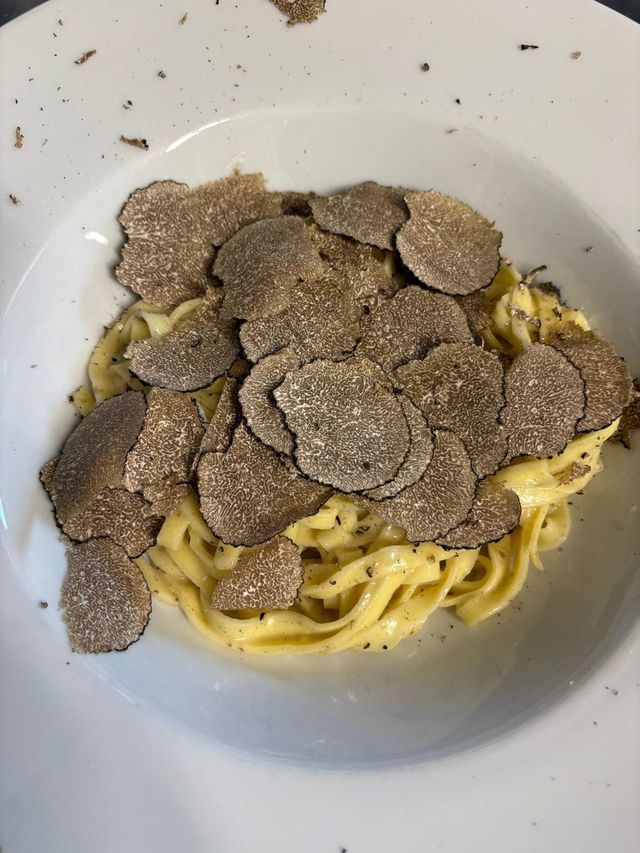 Pasta in una ciotola bianca guarnita con scaglie di tartufo e pepe nero.